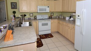 Una cocina con armarios de madera, microondas, estufa, lavamanos y refrigerador.