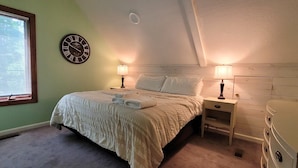 A bedroom with a bed, two bedside tables with lamps, a dresser, a clock on the wall, and a window with blinds.