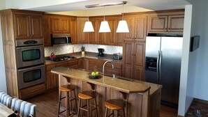 A modern kitchen with wooden cabinets, stainless steel appliances, a granite countertop, and three bar stools.