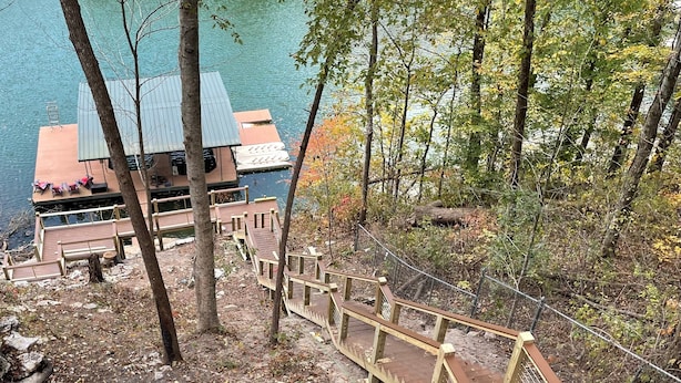A wooden staircase leading to a dock with a metal railing, surrounded by trees and a body of water.