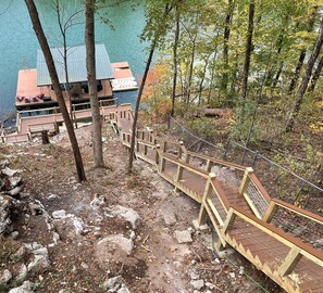 A wooden staircase leading to a dock with a metal railing, surrounded by trees and a body of water.