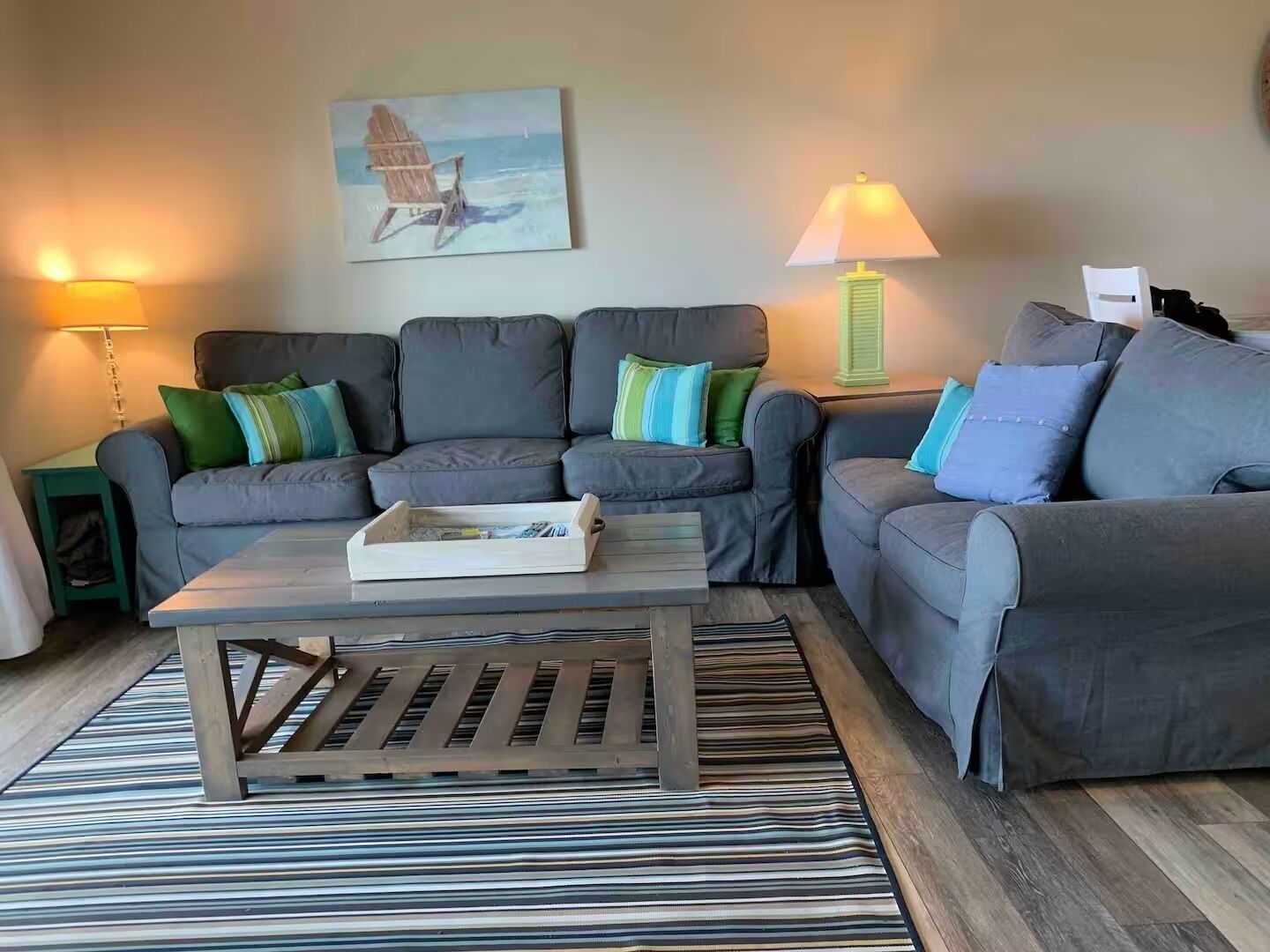 Un salon avec deux canapés gris, une table basse en bois et des tapis à rayures.