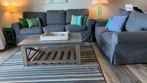 A living room with two grey sofas, a wooden coffee table, and striped rugs. - Stunning 2BR/2BA Oceanfront Condo (Carolina Beach)