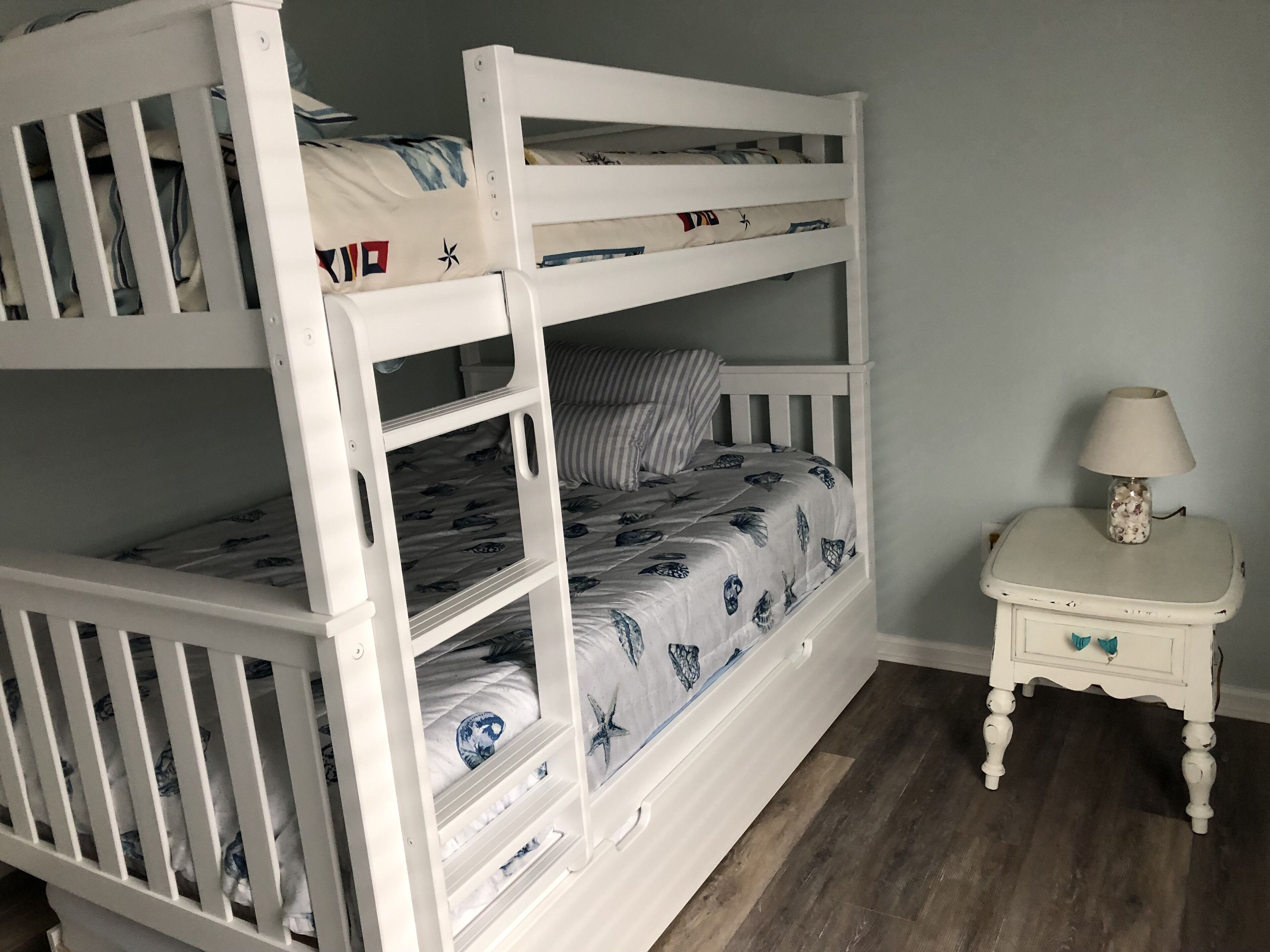 A bunk bed with a patterned bedspread, a bedside table with a lamp, and a wooden floor.