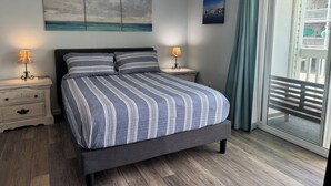 A bedroom with a bed, two bedside tables, a ceiling fan, and a view through a sliding glass door. - Stunning 2BR/2BA Oceanfront Condo (Carolina Beach)