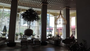 Un hall d’entrée spacieux, doté de grandes fenêtres, d’un arbre en pot placé au centre et de mobilier moderne.