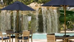 Un espace aménagé au bord de la piscine, avec des tables et des chaises, une cascade et une végétation luxuriante.