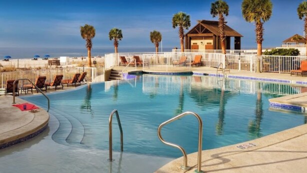 A pool with lounge chairs and umbrellas, a palm tree, and a building with a beach view. - 12th Fl.Remodel 2021, East Wrap Ard View, 2br, Slps7; NEW one vrbo.com/2380847 (Orange Beach)