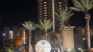 A hotel entrance with a large illuminated sign reading 'ESCAPES! The Showers,' surrounded by palm trees and a water feature. - 12th Fl.Remodel 2021, East Wrap Ard View, 2br, Slps7; NEW one vrbo.com/2380847 (Orange Beach)
