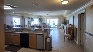A spacious kitchen with a large island, a dishwasher, and a refrigerator. There is a dining area with a table and chairs, and a living room with a sofa and a coffee table. - 12th Fl.Remodel 2021, East Wrap Ard View, 2br, Slps7; NEW one vrbo.com/2380847 (Orange Beach)