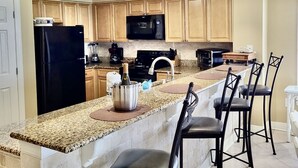 A kitchen with wooden cabinets, a black refrigerator, a microwave, and a granite countertop. - 12th Fl.Remodel 2021, East Wrap Ard View, 2br, Slps7; NEW one vrbo.com/2380847 (Orange Beach)
