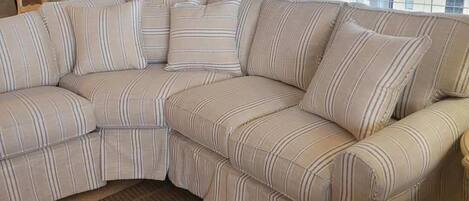 A L-shaped sectional sofa with striped cushions, a brown woven rug, a tall palm tree, and a city view through large windows.