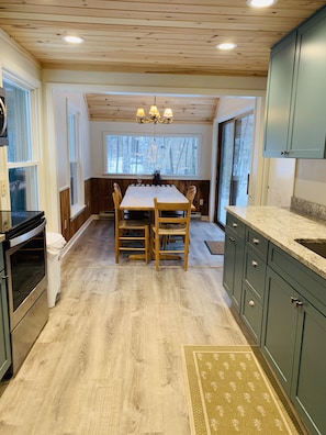 Enjoy meals in this kitchen with a central island, sink, and dining table offering a view of the surrounding trees.