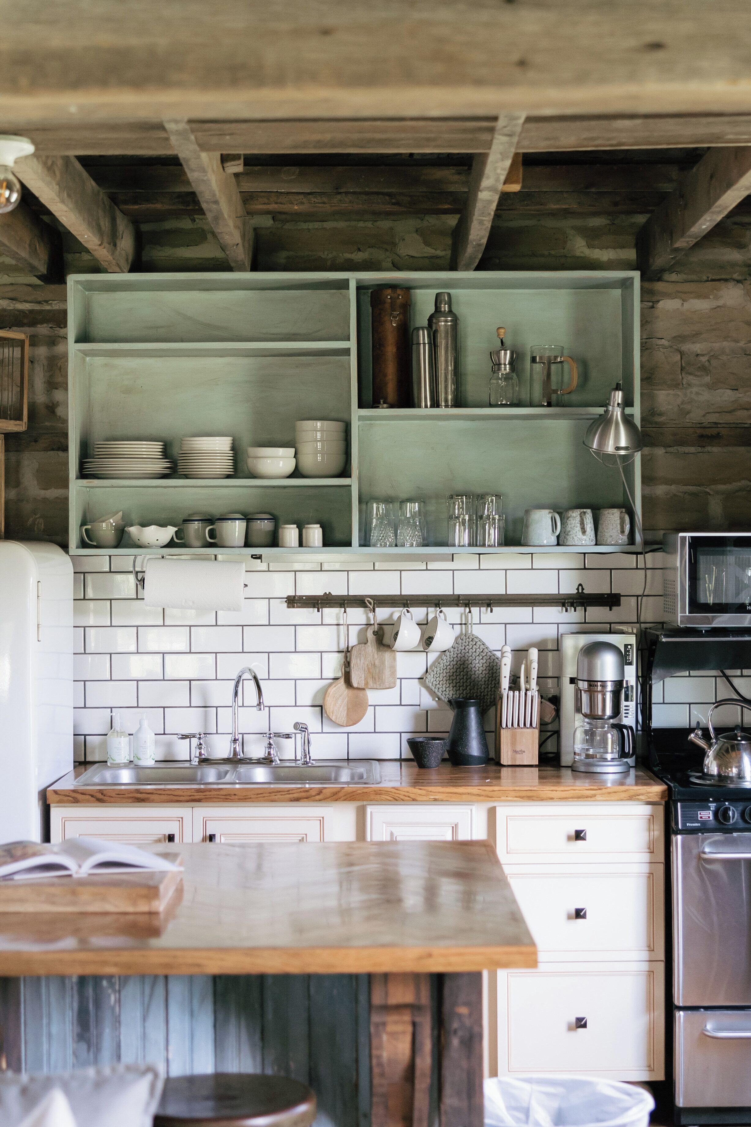 A kitchen with white tiled backsplash, wooden shelves, and a wooden countertop.