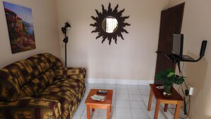 A living room with a patterned sofa, a small wooden table, a TV mounted on the wall, and a potted plant. - Wish Willy Riverview Cabana (Santa Elena)