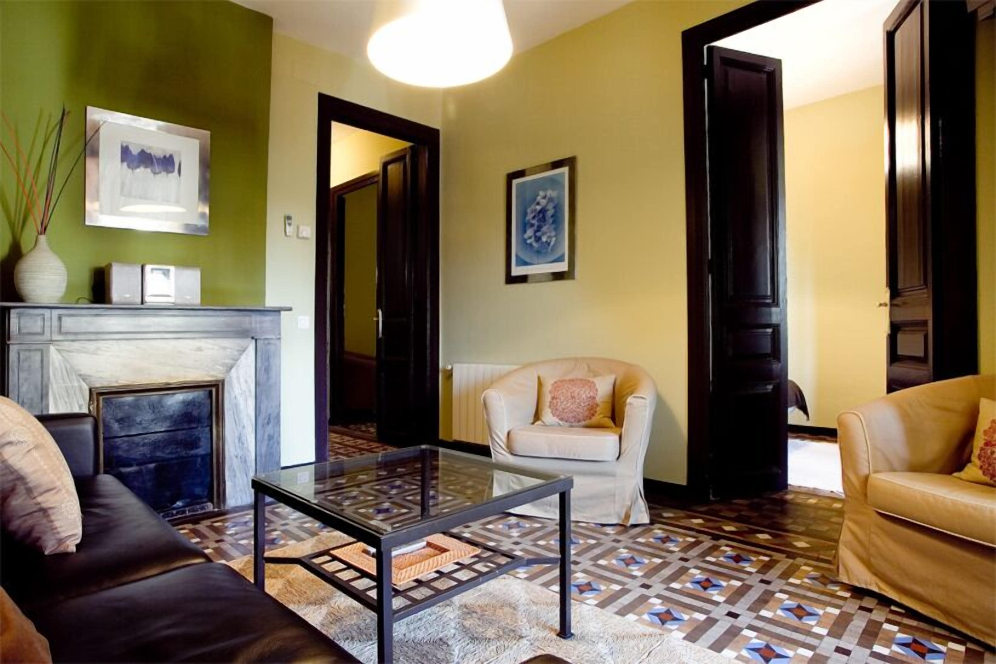 Un salon avec une cheminée, une table basse en verre, un canapé et un tapis à motifs.