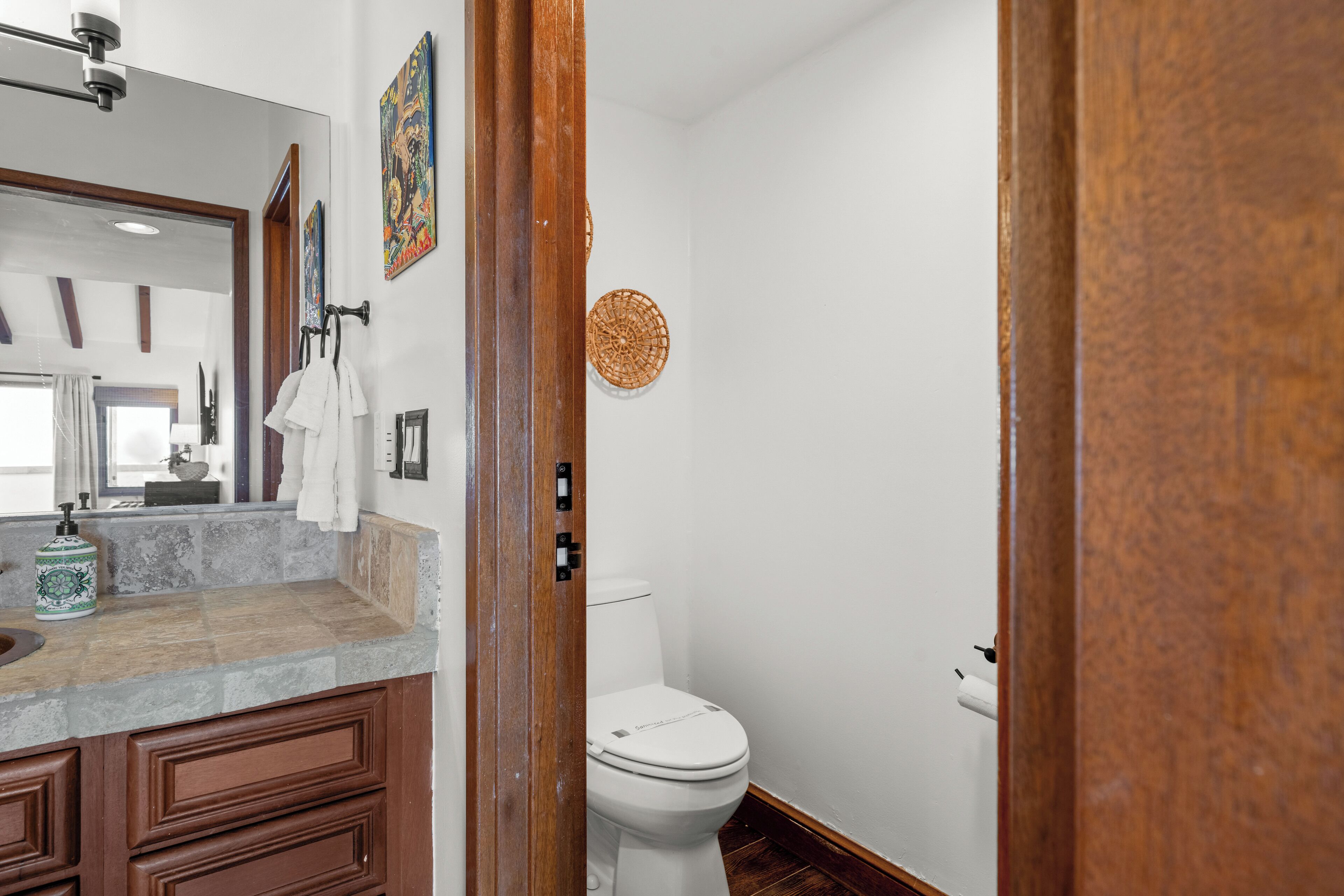 A bathroom with a white toilet, a wooden cabinet, a mirror, and a decorative wall hanging.