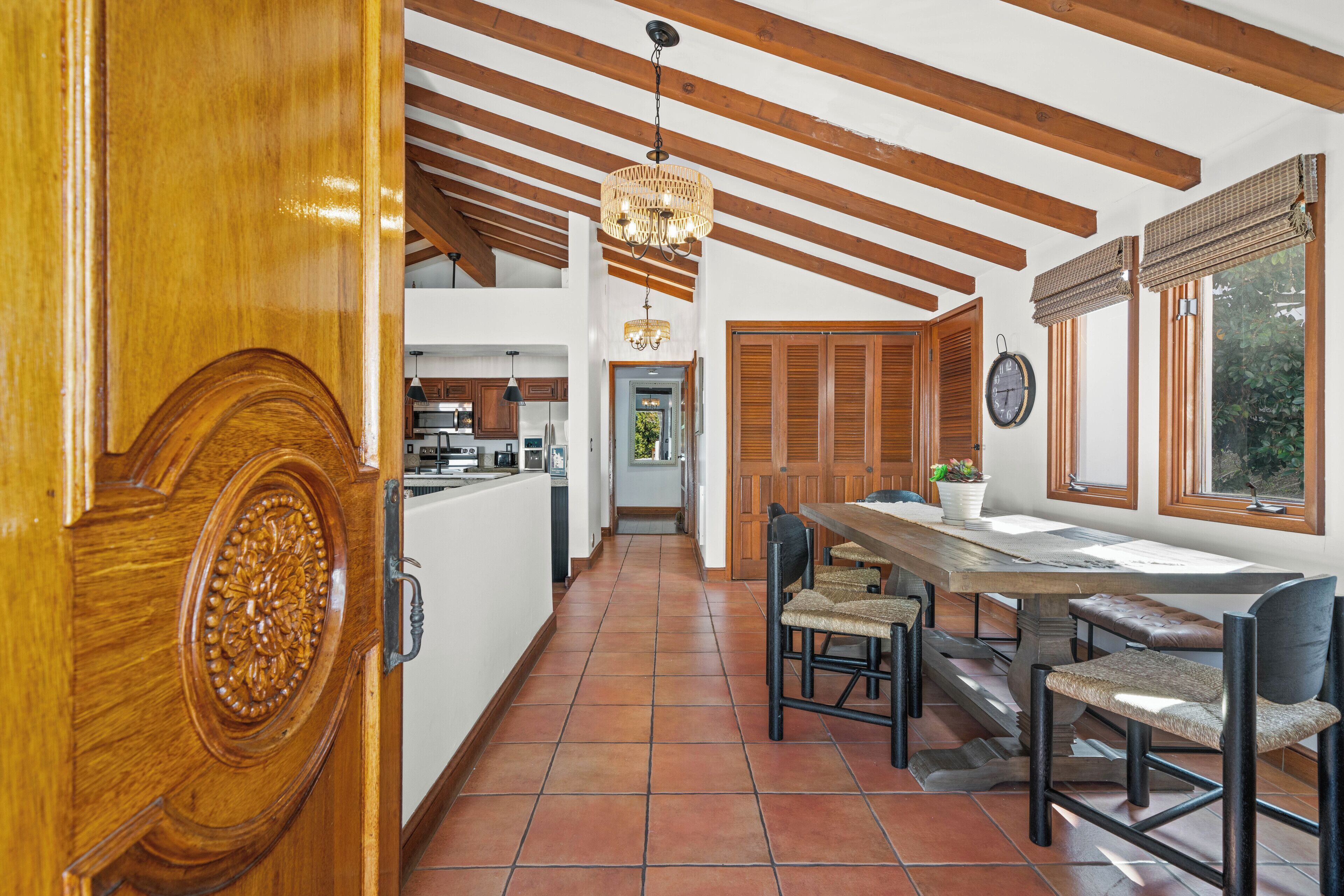 A spacious kitchen with wooden beams, a dining area with a large table and chairs, and a view of the outdoors through windows with wooden shutters.