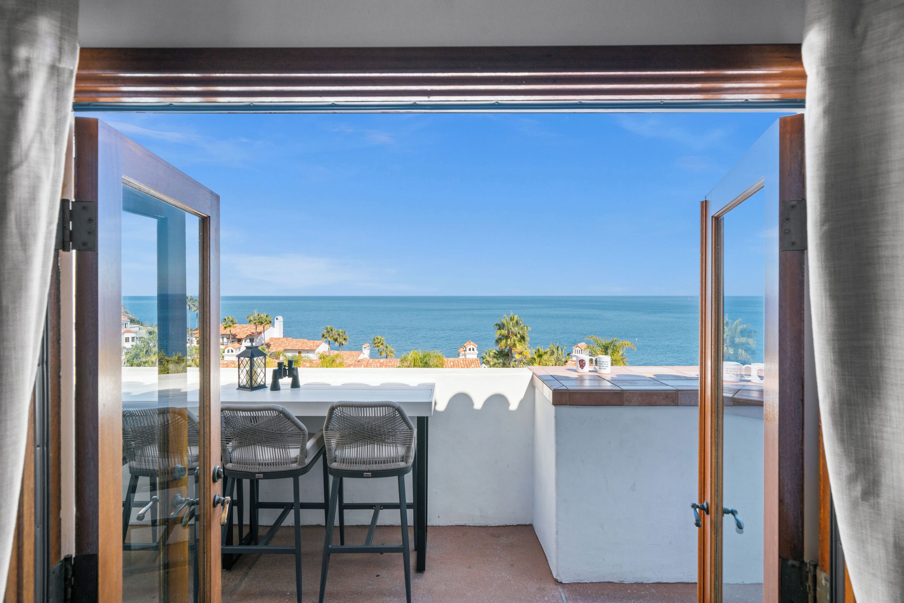 Een balkon met uitzicht op de oceaan, twee rieten stoelen en een tafel met enkele spullen erop.
