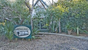 Un panneau indiquant le « Chemin de Surfin », avec un sentier menant à une maison entourée d’arbres et de plantes.