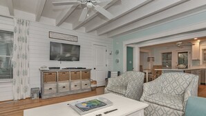 Un salon avec une table basse blanche, des fauteuils à motifs, un téléviseur et un ventilateur de plafond.