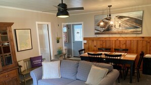 A living room with a gray sofa, wooden dining table, and chairs. There is a wooden cabinet and a framed picture on the wall. - Harbor House Cottage located in the heart of Ephraim! (Ephraim)