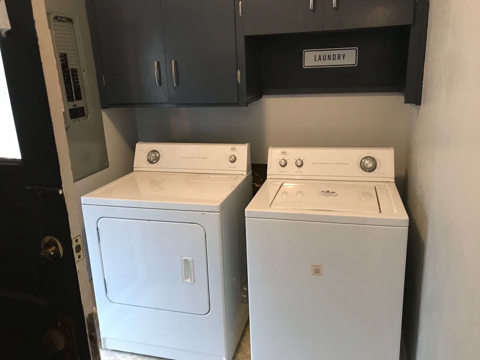 A laundry room with two white front-loading washers and a dark-colored cabinet above them.