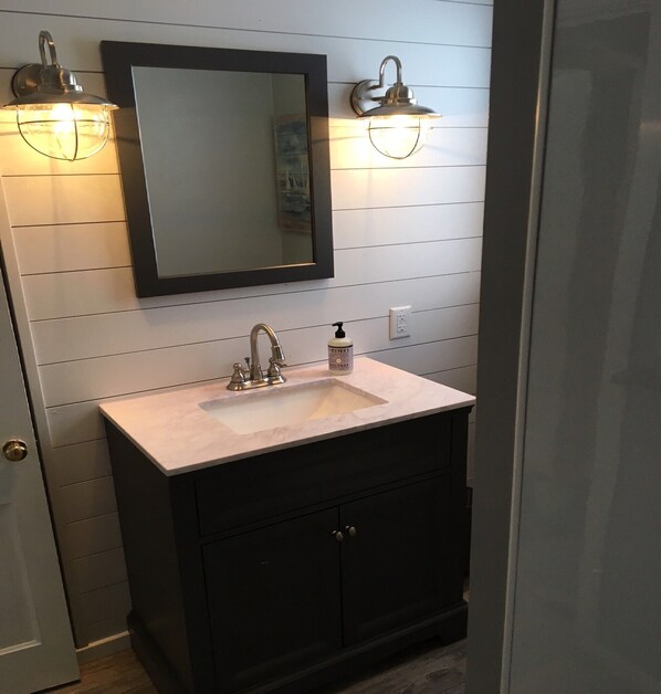 A bathroom with a white sink, dark cabinets, a mirror, and wall-mounted lights.