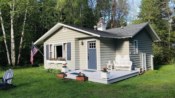 A small, single-story house with a front porch, a flag, and a small garden area. - Harbor House Cottage located in the heart of Ephraim! (Ephraim)