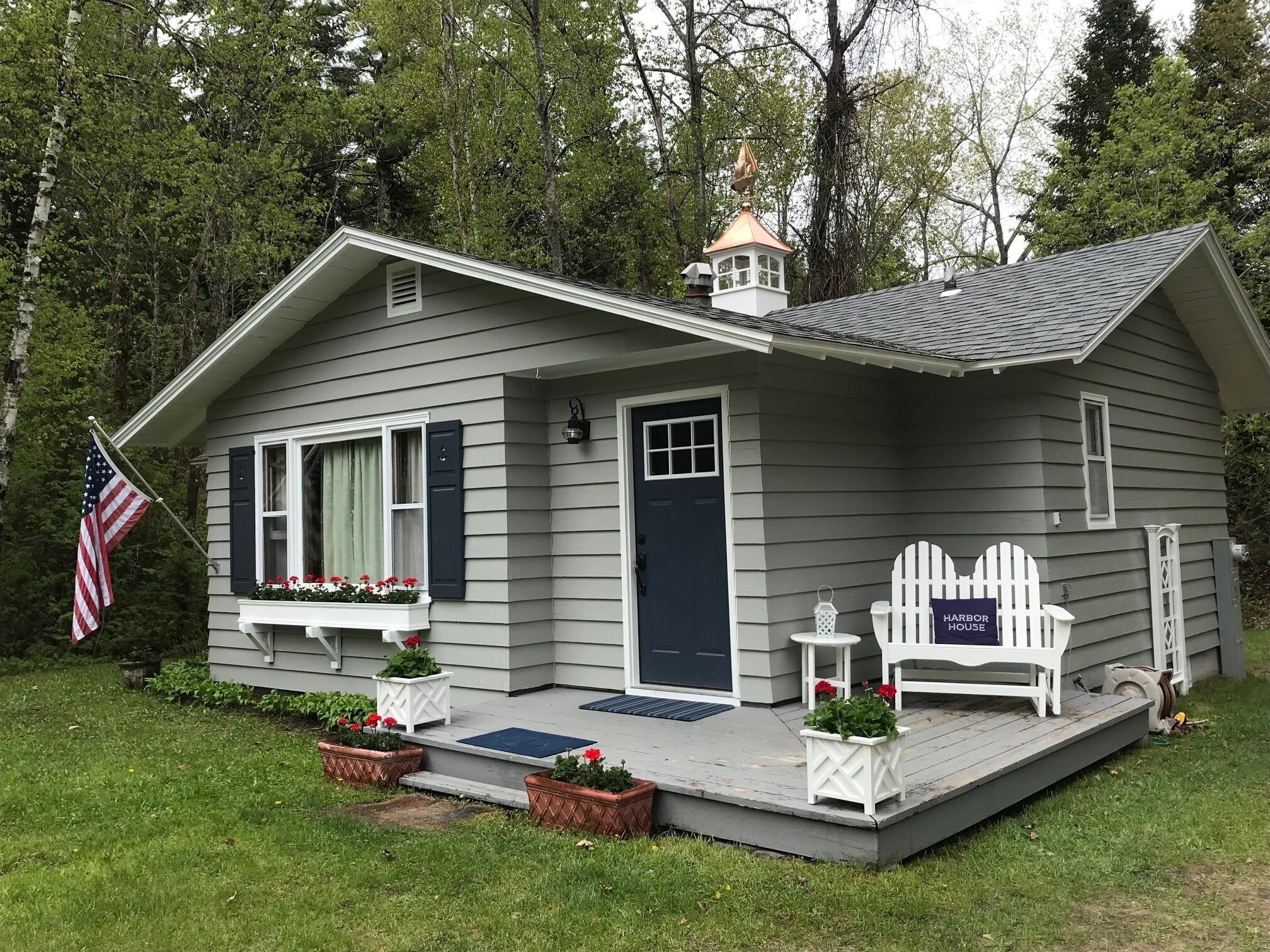 Een klein, gelijkvloers huis met een donkerblauwe deur, een klein portaaltje met een witte stoel, en een bordje met de tekst 'Harbor House'.