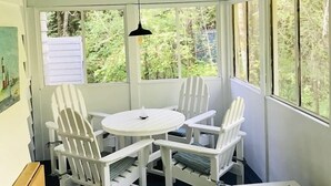 A covered patio with a round table and four Adirondack chairs, large windows, and a hanging pendant light. - Harbor House Cottage located in the heart of Ephraim! (Ephraim)