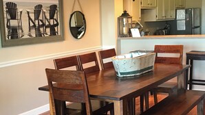 A dining room with a wooden table and chairs, a chandelier, a framed artwork, and a kitchen in the background. - Fantastic place to make memories. Great ocean view condo for fun & “GOOD TIMES” (Pawleys Island)