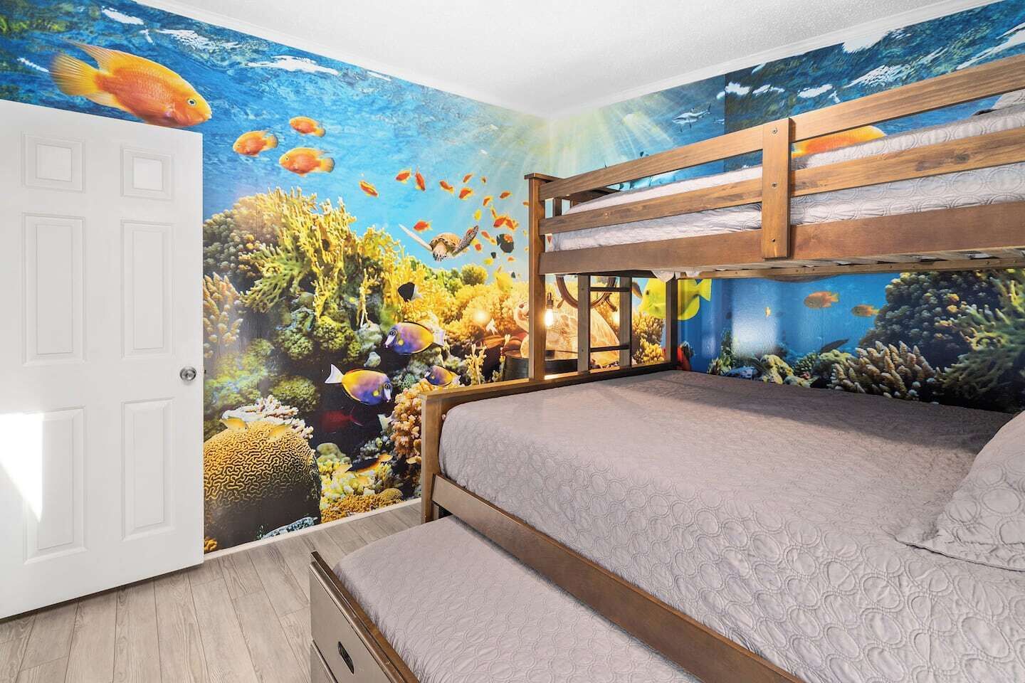 A bedroom with a bunk bed, a mural of an underwater scene, and a door.