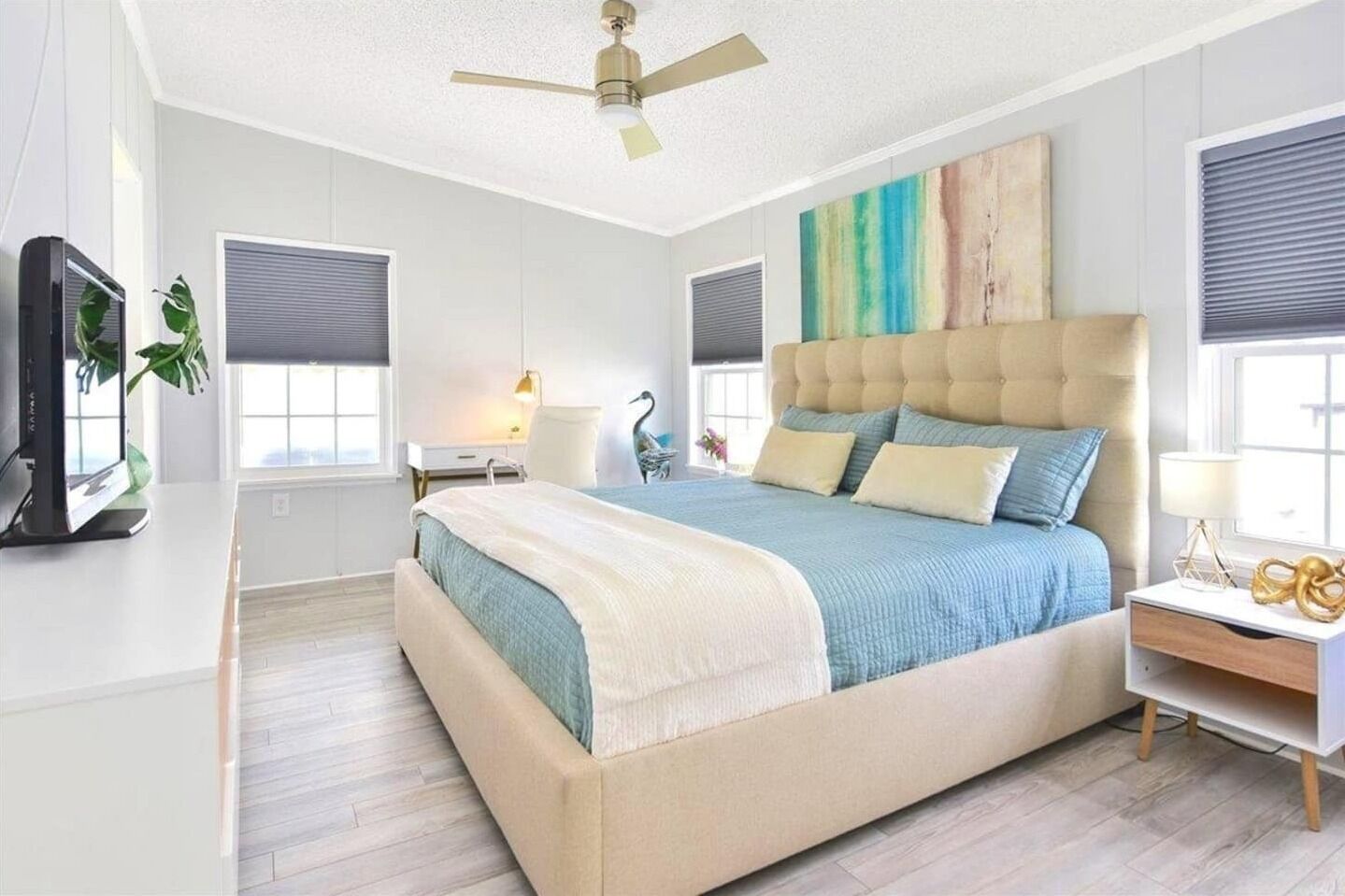 A modern bedroom with a large bed, a ceiling fan, a desk, and a TV.