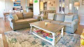 A living room with a sofa, a coffee table with books, a rug, and a dining area with chairs and a table.