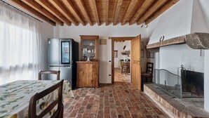 Una cocina rústica con suelo de ladrillo, vigas de madera en el techo, un refrigerador, un armario y una chimenea.