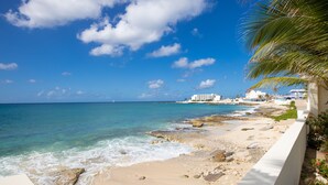 A beach with clear blue water, a sandy shore, and a white building in the background. - BEACHFRONT DESIGN VILLA (Beacon Hill)
