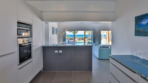 A modern kitchen with a central island, built-in oven, and a view of the pool and beach. - BEACHFRONT DESIGN VILLA (Beacon Hill)