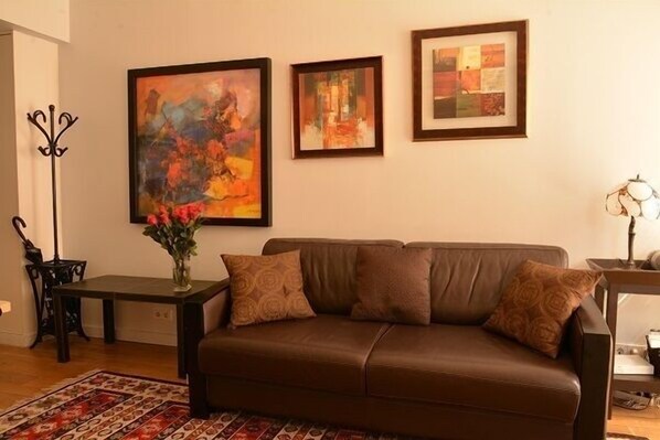 A living room with a brown leather sofa, a patterned rug, and three framed artworks on the wall.