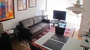 A living room with a leather sofa, a flat-screen TV, a dining table with placemats, and a patterned rug. - Lovely Modern Apartment - Walk to Champs Elysées - Best Area! (Paris)