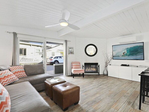 Un salon moderne avec un canapé, un pouf, une cheminée et un téléviseur diffusant une image d’un surfeur.