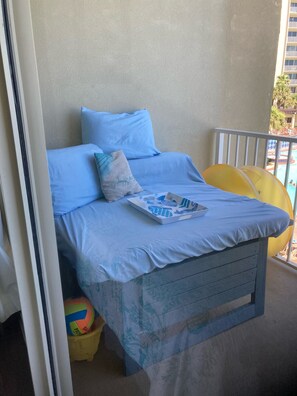 Un balcon avec un lit, des oreillers, un livre et une chaise jaune.