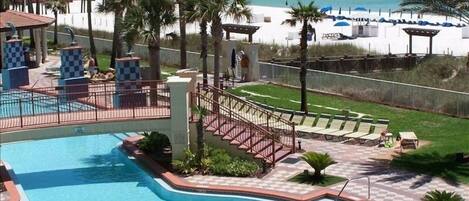 A pool area with a view of the beach, palm trees, and lounge chairs.
