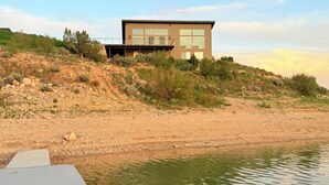 Een modern huis met een plat dak, grote ramen en een terras dat uitsteekt over een wateroppervlak.