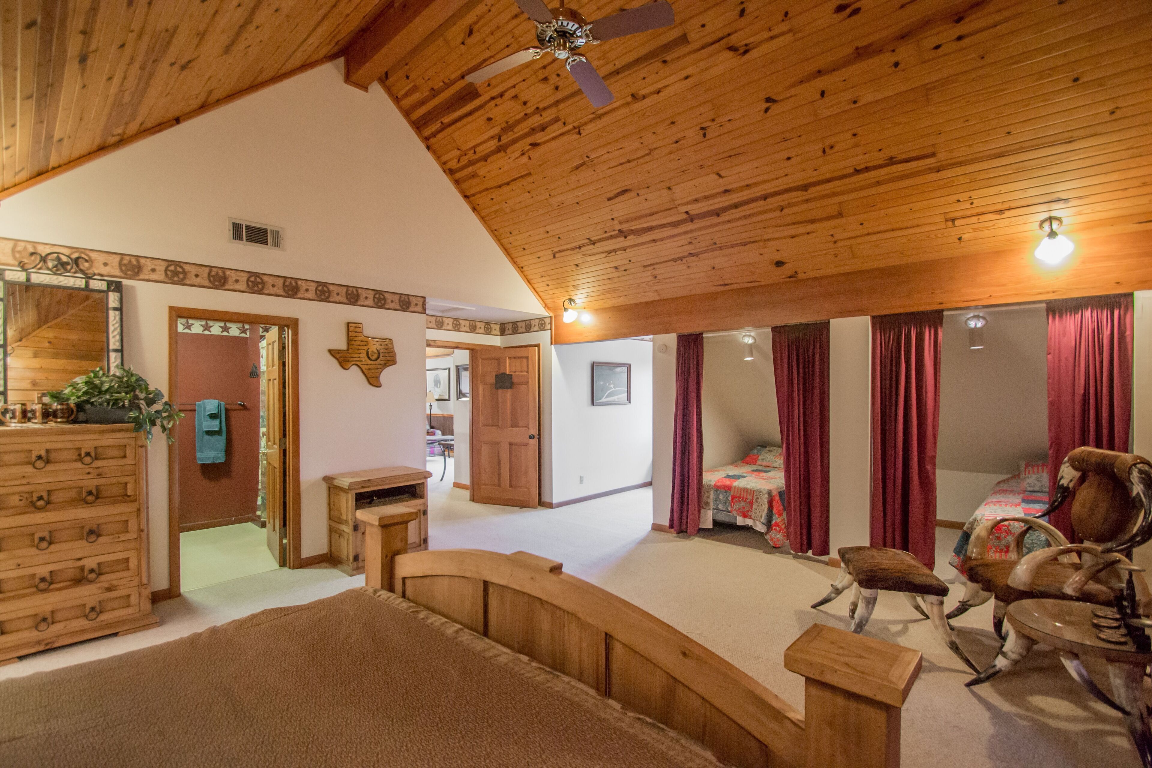 A spacious bedroom with a wooden ceiling, a large bed, a rocking chair, and a desk.