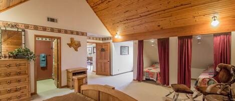 A spacious bedroom with a wooden ceiling, a large bed, a rocking chair, and a desk.