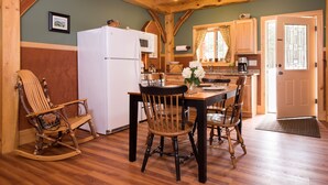 Une cuisine rustique avec des poutres en bois, un réfrigérateur blanc, une table à manger avec des chaises et un fauteuil à bascule.