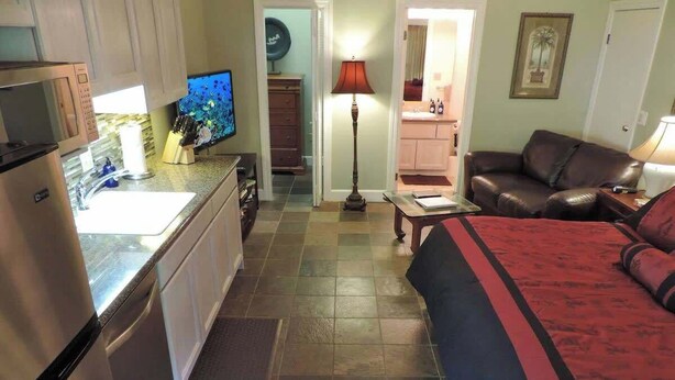 Cocina compacta con microondas, lavamanos y televisor. Hay un comedor con mesa y sillas, además de una sala de estar con sofá y lámpara.