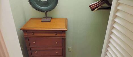 A small bathroom with a wooden dresser, a wall-mounted mirror, and a shelf with folded towels.