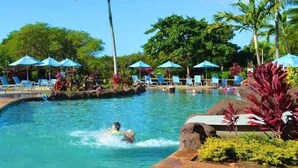 Una piscina con sillas de descanso y sombrillas, rodeada de palmeras y plantas tropicales.